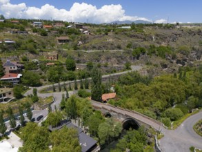 Idyllic village landscape amidst hills, near a river, with clear clouds in the sky, aerial view,