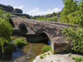 Old stone bridge with two arches over a flowing river under a clear sky, aerial view, bridge from