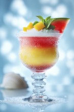 A colorful layered cocktail with mango, watermelon, and mint garnish, presented in a elegant glass,