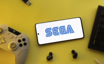 Dhaka, Bangladesh- 13 Sep 2025: Smartphone with Sega logo, game controller, and earbuds on a yellow