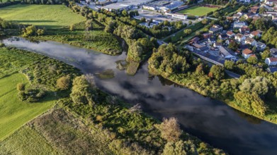 An idyllic landscape shows a gently flowing river, surrounded by lush vegetation and a small town