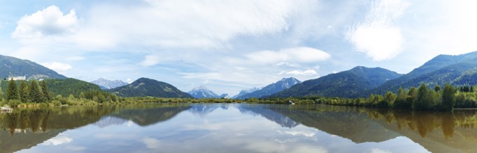 Panoramic lake reflects the surrounding mountains and the slightly cloudy sky, Admont, Styria,