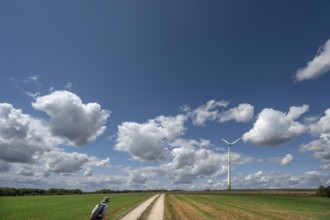 Hiker on a country lane in Franconian landscape, a windmill behind, cloudy sky, Karsberg, Upper
