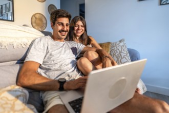 Young couple relaxing on sofa, enjoying streaming movie on laptop in cozy living room, illuminated