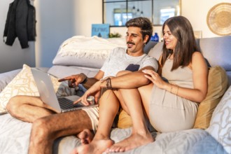 Young couple relaxing on comfortable sofa, browsing internet on laptop, enjoying time together in