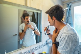 Caucasian man trimming his mustache with an electric razor while looking in the bathroom mirror