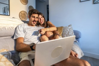Young couple enjoying a movie on their laptop, laughing and having a good time together on the sofa
