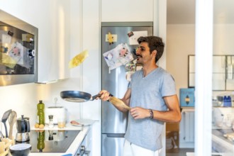 Young man flipping a pancake in a modern kitchen, enjoying a leisurely morning preparing breakfast