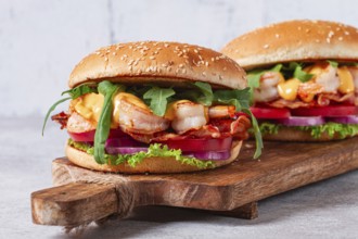 Two shrimp burgers and buns with sesame seeds, bacon, lettuce, tomatoes and onions, On a wooden