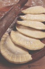 Raw chebureks, mini, on a cutting board, wooden table, close-up, no people