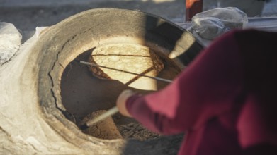 A Turkish woman bakes traditional bread on a clay tandoor oven in a rural village, Hatay, Hatay,