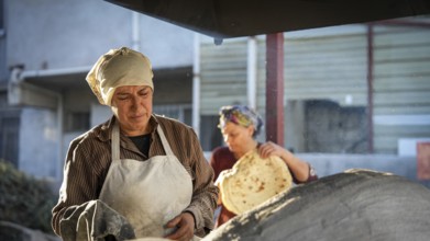 A Turkish woman bakes traditional bread on a clay tandoor oven in a rural village, Hatay, Hatay,
