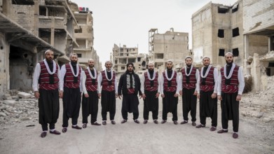 A Syrian traditional Arada troupe pose in traditional attire amid destroyed buildings in a war-torn