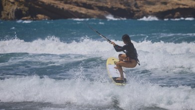 Kitesurfer spraying over waves in the blue sea, rocky coast in the background, Prasonisi, beach,