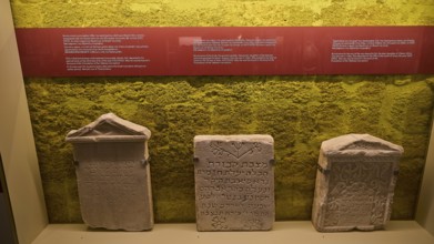 Three ancient Hebrew tombstones in an exhibition with yellow background, Kahal Shalom Synagogue,