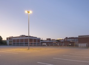 Taking a street lamp on an empty car park in front of an industrial building in the evening,