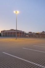 Taking a street lamp on an empty car park in front of an industrial building in the evening,