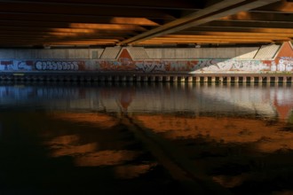 View across the Mittelland Canal to the underside and the graffiti-painted abutment of a bridge on