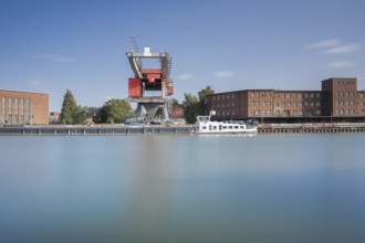 View over the Mittelland Canal to an industrial building and a crane in front of a ship, long