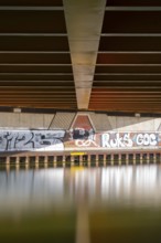View across the Mittelland Canal to the underside and the graffiti-painted abutment of a bridge on
