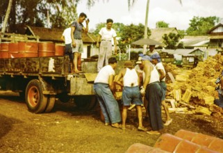 Male workers loading metal fuel drums onto back of lorry in timber yard, Johor Bahru, Johor,