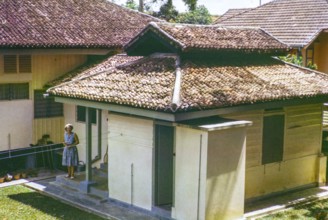 British expatriate woman standing outside next to quarters of her Amha domestic servant, 3 Jalan