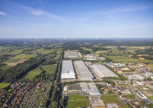 Industrial area with large factory buildings, surrounded by fields and forest under a blue sky,