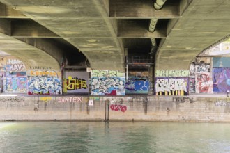 Under a bridge with various colourful graffiti over a river, Am Donaukanal Innere Stadt Vienna