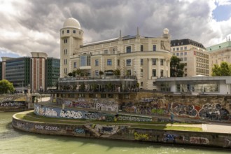 A historic building on the riverbank with graffiti on the wall and a cloudy sky Urania Ringstraße