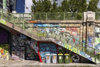 Various graffiti artworks on a concrete wall next to stairs and rubbish bins, Am Donaukanal Innere