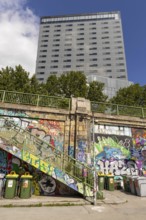 A modern high-rise building with a staircase in the foreground full of graffiti under a blue sky
