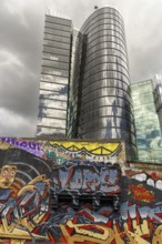 A modern high-rise building with a reflective glass façade and colourful graffiti in the foreground