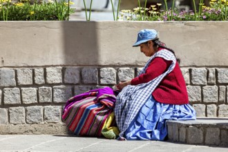 Woman in traditional dress sitting next to a stone wall and resting, Traditionally dressed woman in