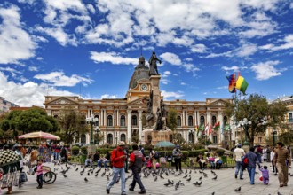 Lively square with pigeons and people in front of a historic building and a statue under a blue