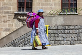 A woman with a colourful bag and traditional clothes walks along a stone wall, Traditionally