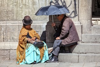 An elderly woman in traditional dress sitting and chatting with a man under an sunshade, A woman