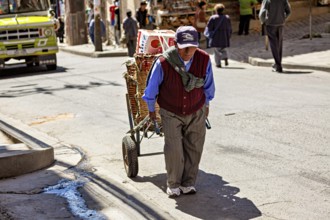 An elderly man pulls a handcart through a sunny city street, A man pulls a handcart through the