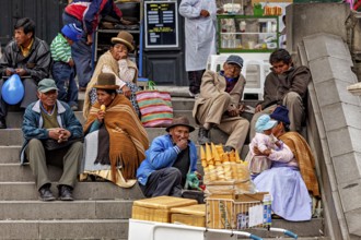 People in traditional dress sit on a staircase and talk near a market stall with ice cream,