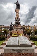 A monument with an imposing statue surrounded by a dramatic sky and historic buildings, monument in