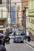 Busy city street with a blue bus and many people during the day in the middle of tall buildings, A