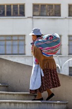 A woman carries a colourful bag and climbs a staircase in front of a building view, Traditionally