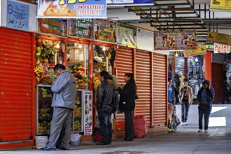 Busy market with people buying fresh vegetables and other food, small shops and restaurants in the