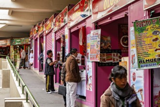 Row of pink market stalls with colourful signs, people ordering food, small shops and restaurants