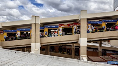 Long view of the upper floor of a market with colourful stalls and many customers, Small shops and