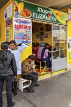 Small food stall with yellow walls, people sitting and eating, menu posters on the wall, Small
