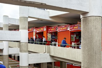 People walk through the upper floors of a modern market with red facades, Small shops and