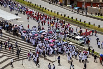 Large gathering of people with umbrellas on a city street, flanked by buildings, A demonstration in