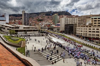 Overview of busy urban environment with crowds, modern buildings and a mountain backdrop, A