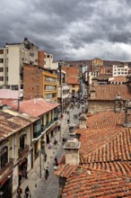 Historic city view with red tiled roofs under a cloudy sky, people in the streets of La Paz in