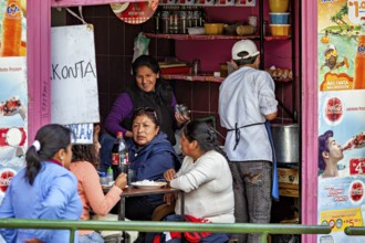 People enjoy their meals in the middle of a lively street snack bar, surrounded by colourful
